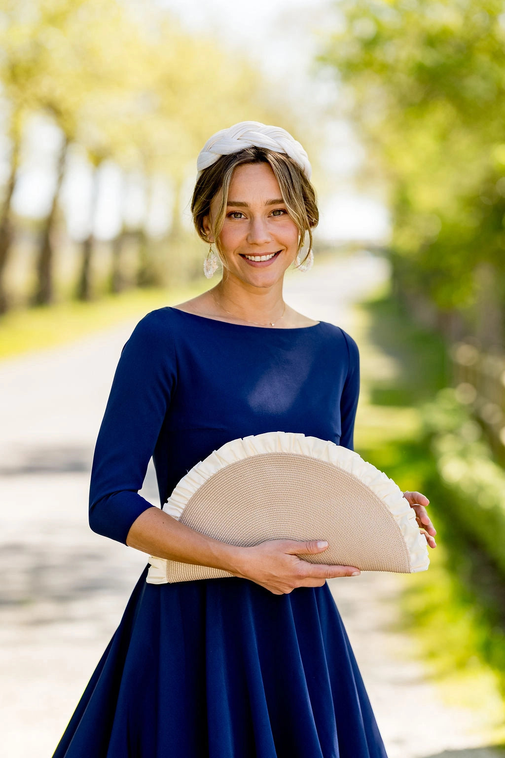 Jeune femme habillée d'une robe bleue marine portant une pochette en demie lune beige dont dépassent des fronces de couleur crème. Créé par Bellemond.