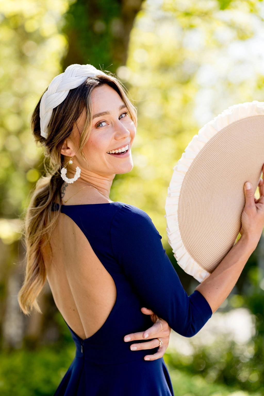 Jeune femme se retournant et utilisant sa pochette de forme demie lune comme un éventail. Les couleurs de la pochette sont beige et crème. Créé par Bellemond.