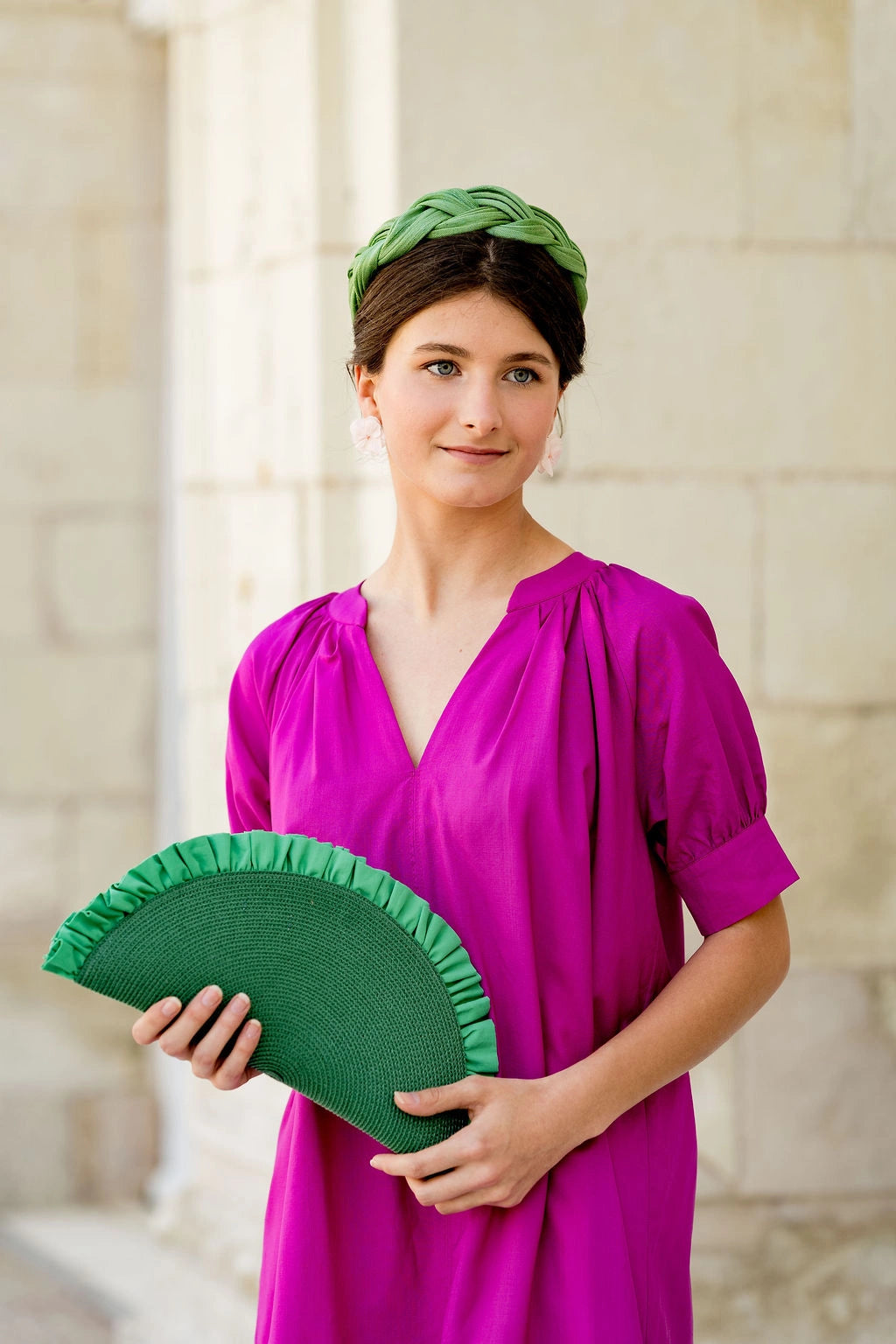 Jeune femme habillée de fuchsia portant une pochette verte avec des fronces qui dépassent. Créé par Bellemond.
