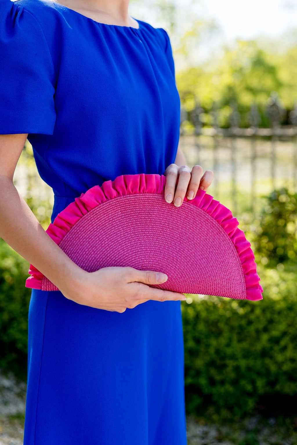 Jeune femme habillée d'une robe bleue roi portant une pochette en demie lune avec des fronces de couleur fuchsia. Créé par Bellemond.