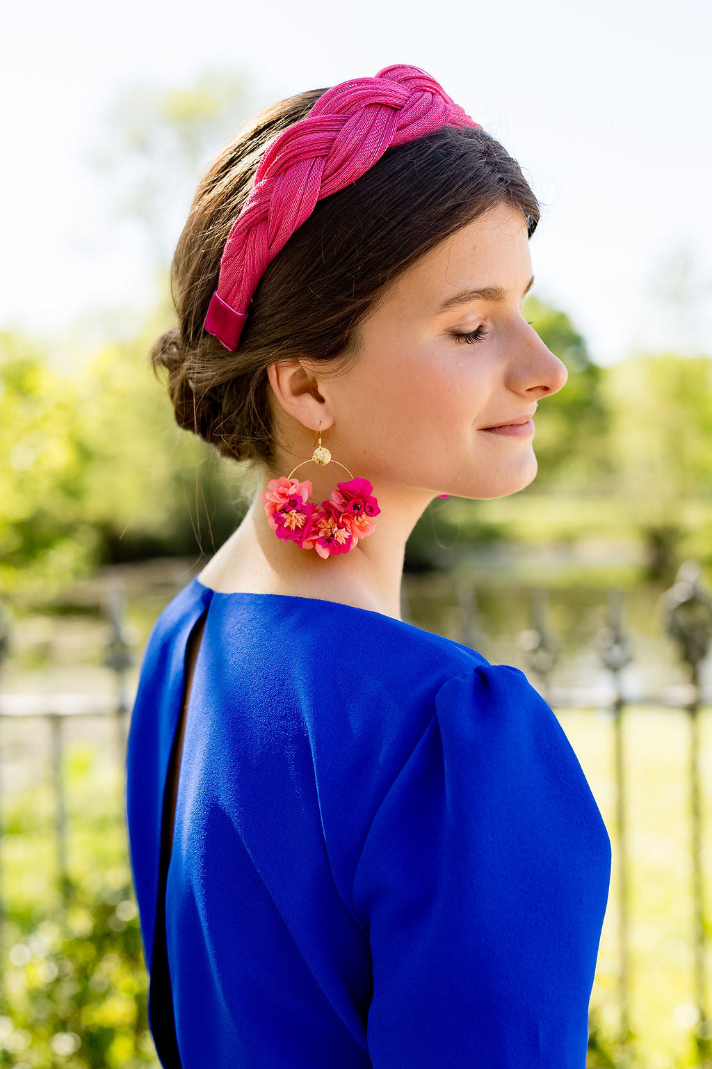 Jeune femme habillée d'une robe bleue roi portant sur la tête un serre-tête de couleur fuchsia. Ce serre-tête est tressé et composé de sinamay. Créé par Bellemond. 