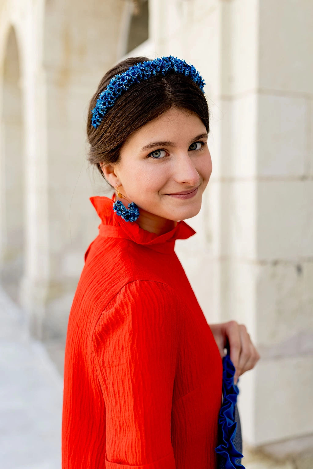 Jeune femme portant une robe rouge coquelicot et ayant dans les cheveux un serre-tête composé de fleurs séchées glixia bleues. Créé par Bellemond.