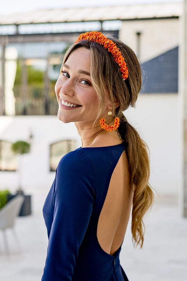 Jeune femme portant une robe bleue marine avec dans les cheveux un serre-tête composé de fleurs glixia oranges. Créé par Bellemond.